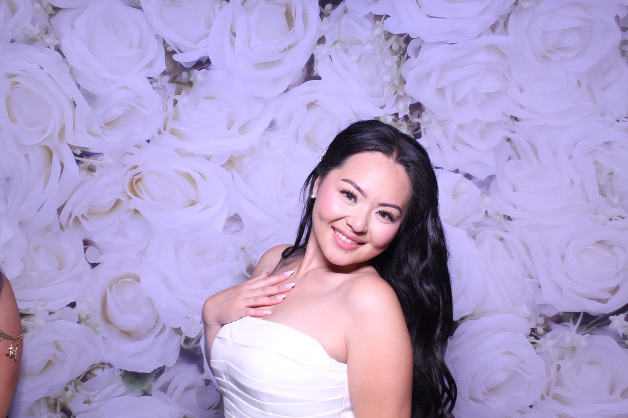 A guest posing against a white rose photo booth backdrop