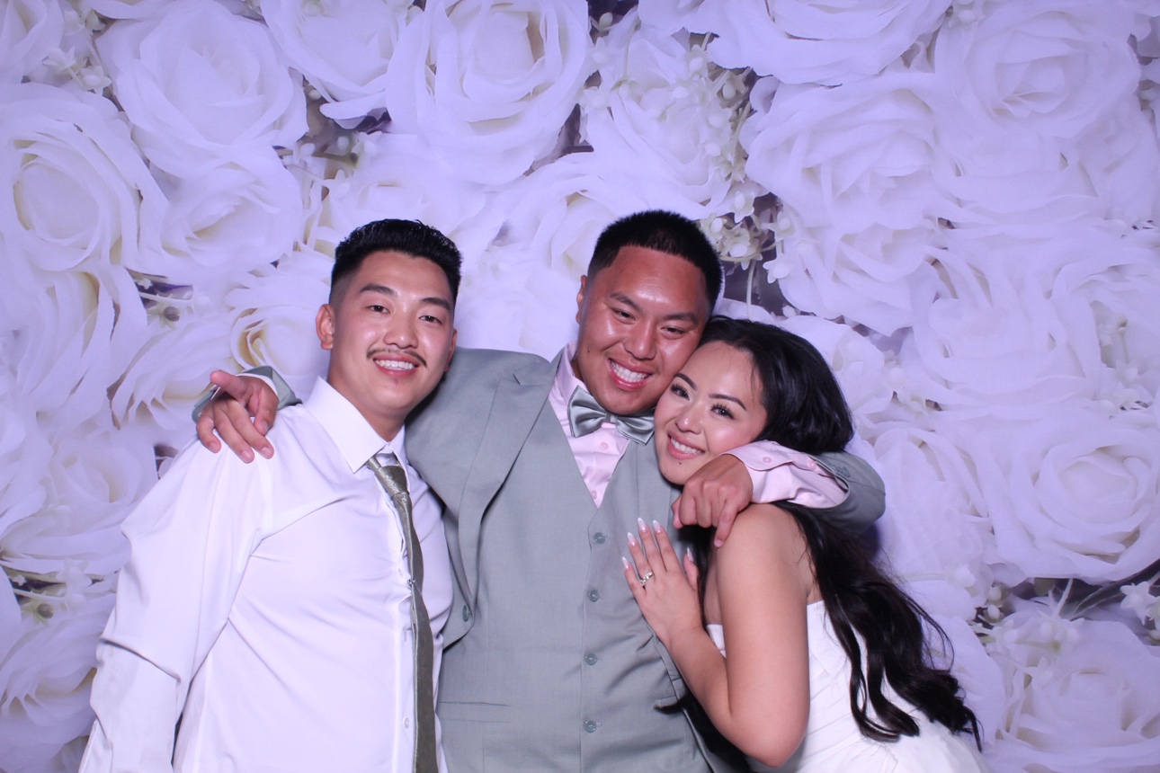 Three guests smiling together against a white rose photo booth backdrop