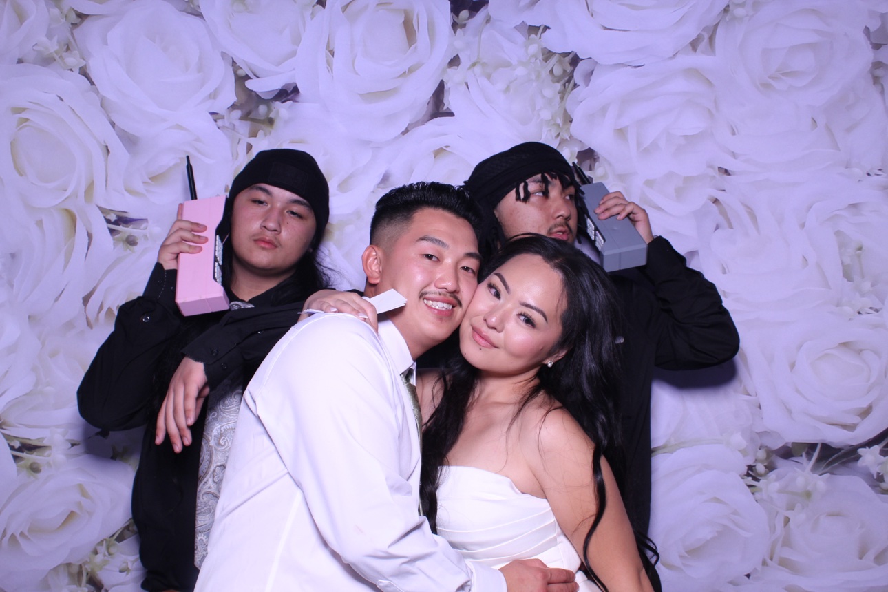 Four guests striking a playful pose against a white rose photo booth backdrop