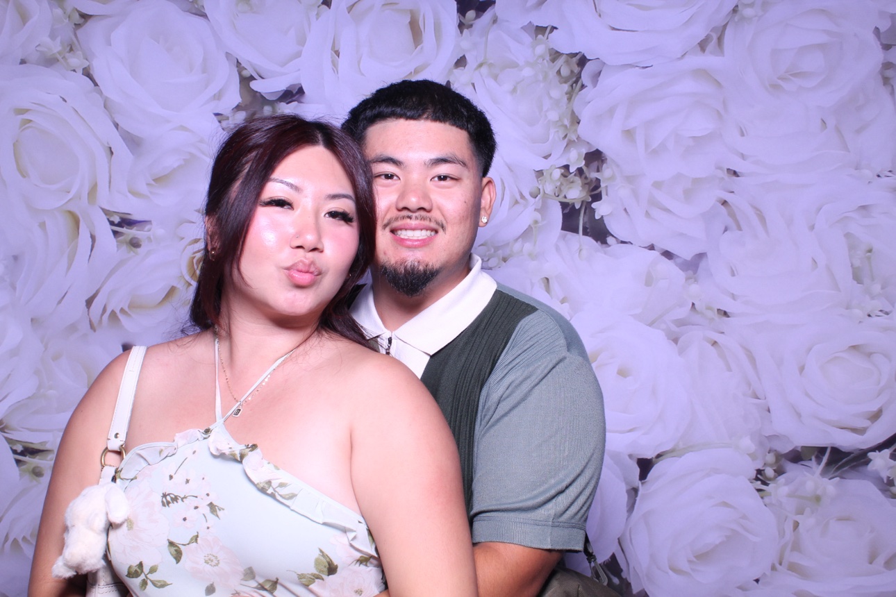 Two guests posing together against a white rose photo booth backdrop