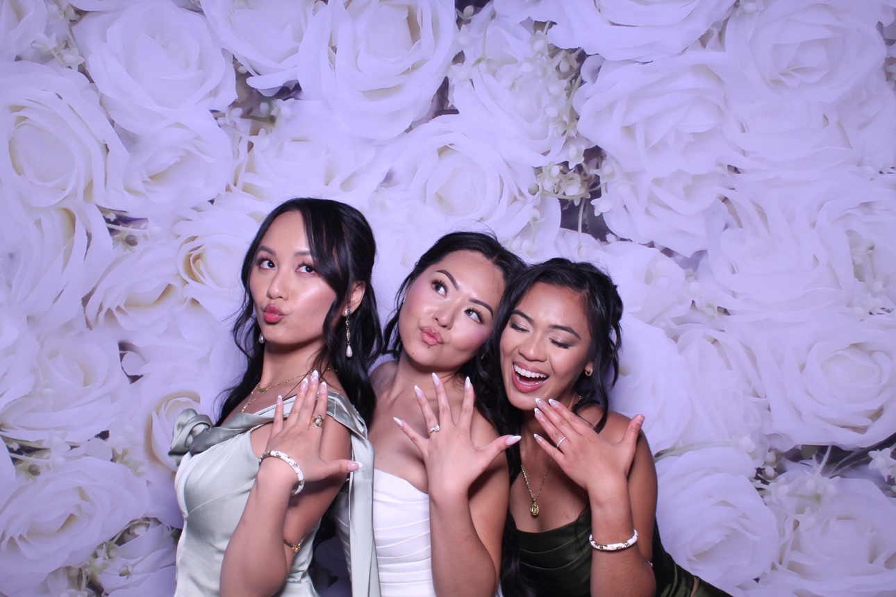 Three guests posing with their hands raised against a white rose photo booth backdrop