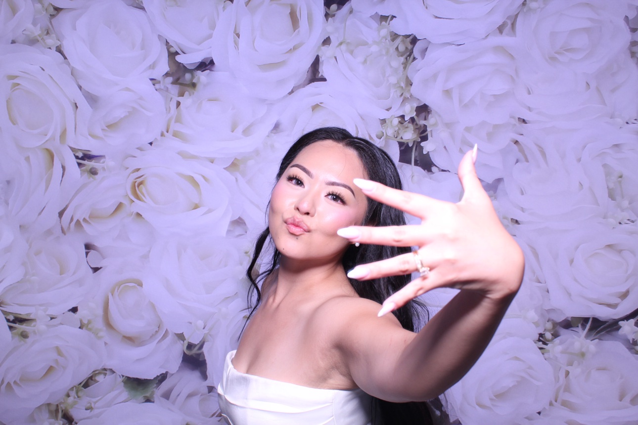 A guest playfully reaching toward the camera against a white rose photo booth backdrop