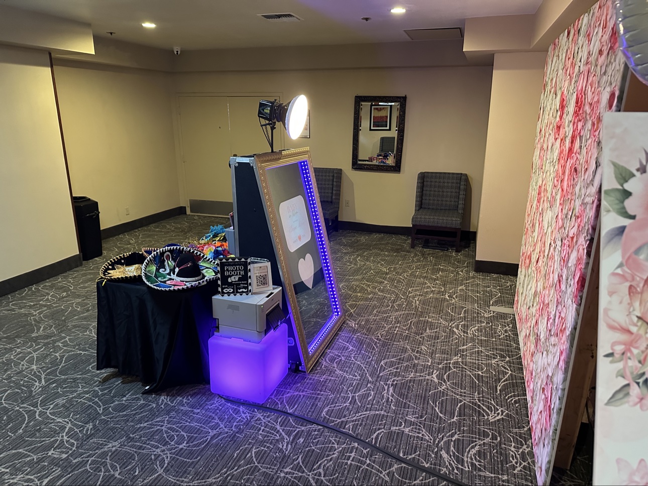 Mirror photo booth with purple lighting, a flower wall, and a table of props
