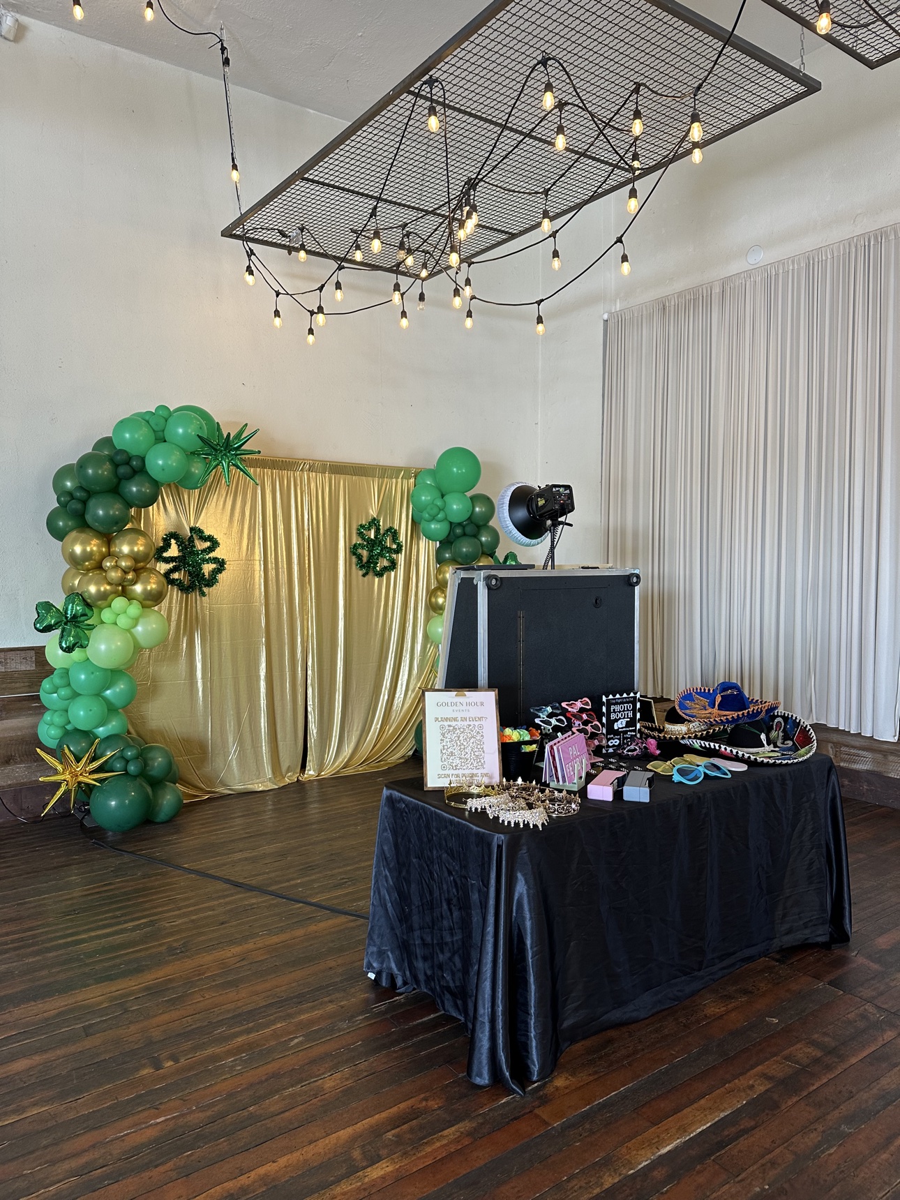 Event setup with a gold curtain, green balloon arch, mirror booth, and props table