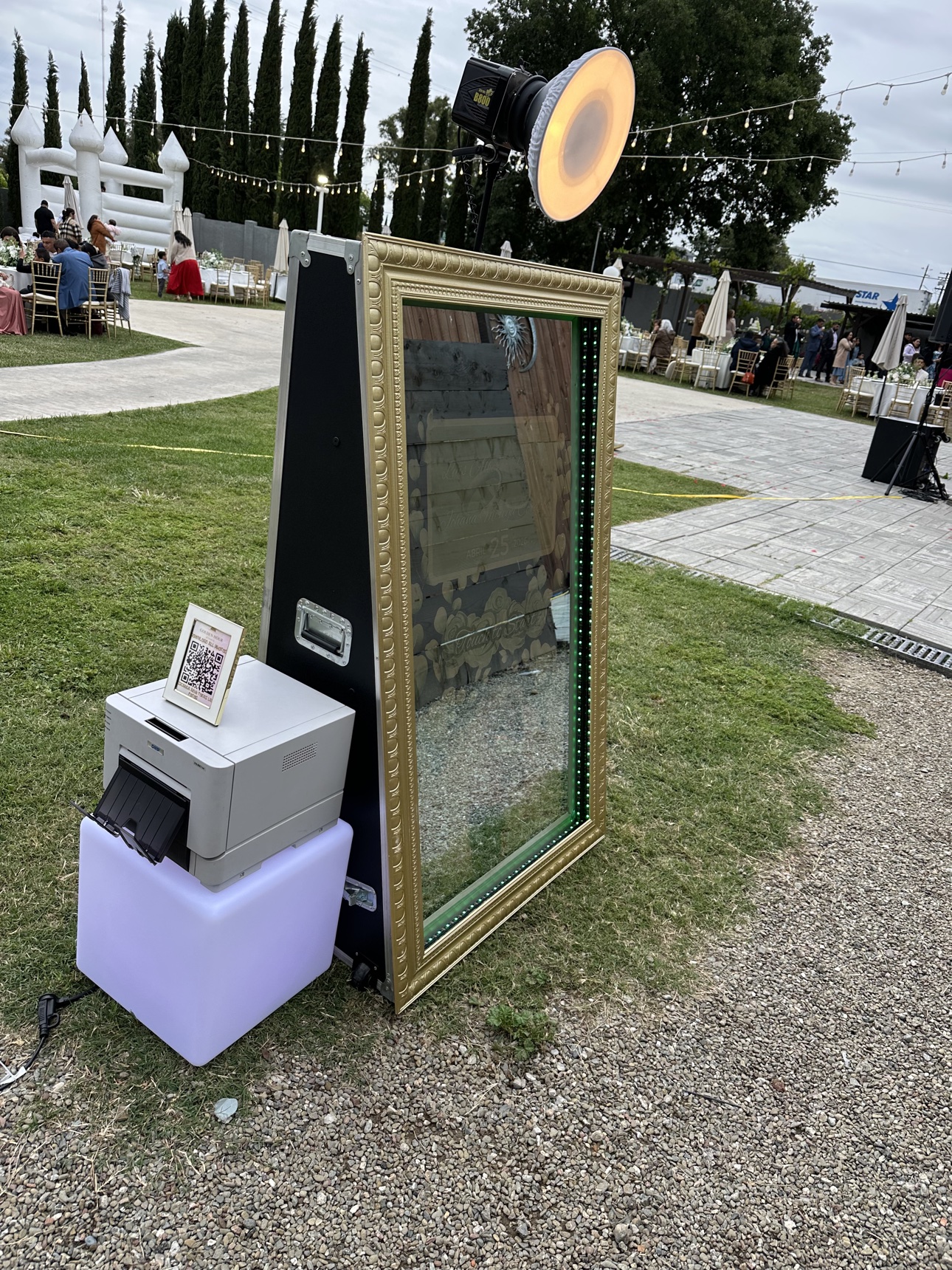 Gold-framed mirror photo booth set up on the grass at an outdoor wedding